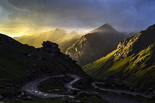 photo of road near mountains under cloudy sky