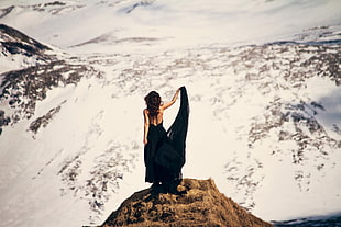 woman stand on brown rock cliff wearing black backless dress