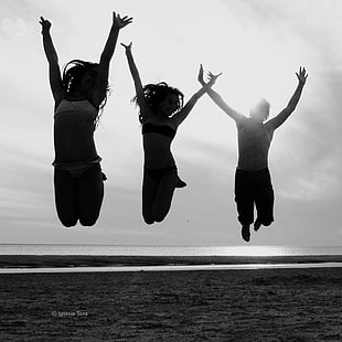 silhouette of three person jumping under cloudy sky during daytime