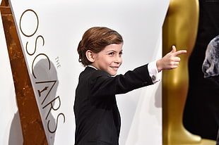 boy in black blazer pointing right hand behind The Oscars wall text
