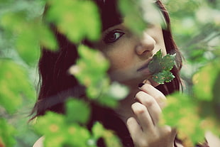 tilt shift lens photography of woman behind green leaves