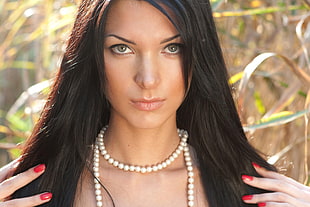 woman wearing pearl necklace in middle of forest during daytime close up photo