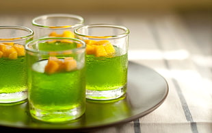 four clear drinking glasses with green liquid on table