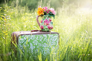 yellow-pink flower bouquet on ceramic vase on travel bag on grass field