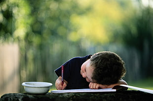 boy writing on paper during daytime