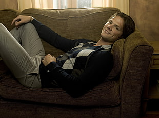 man in white and gray Argyle sweater laying on brown sofa