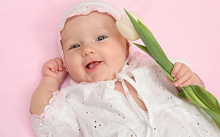 baby wearing white and pink beanie holding beige floral