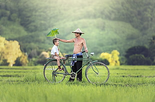 man holding bicycle while boy riding on bicycle back seat HD wallpaper