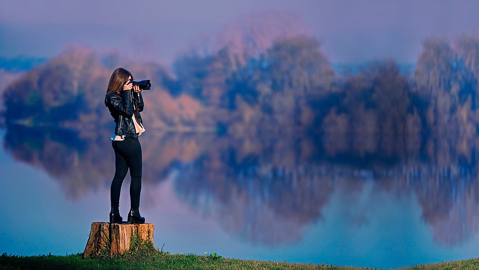woman in black leather jacket standing while taking pictures during daytime HD wallpaper