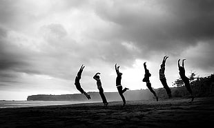 grayscale of six people raising their hands while jumping
