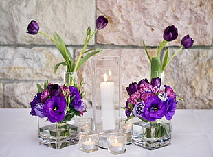 white taper candle between two purple flowers on vase