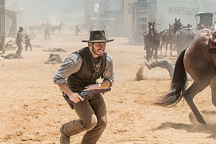 cowboy holding shotgun near brown horse