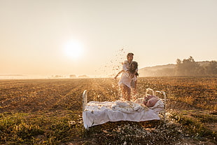 man and woman near white bed on open field during golden hour