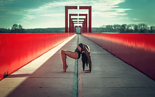 woman in black bending her body on gray bridge