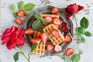 sliced strawberries in gray plate with rose flowers beside