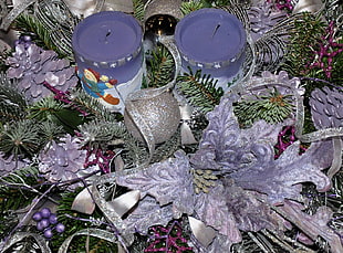 two purple pillar candle in middle of green wreath surrounded by pinecones and glittered Christmas baubles