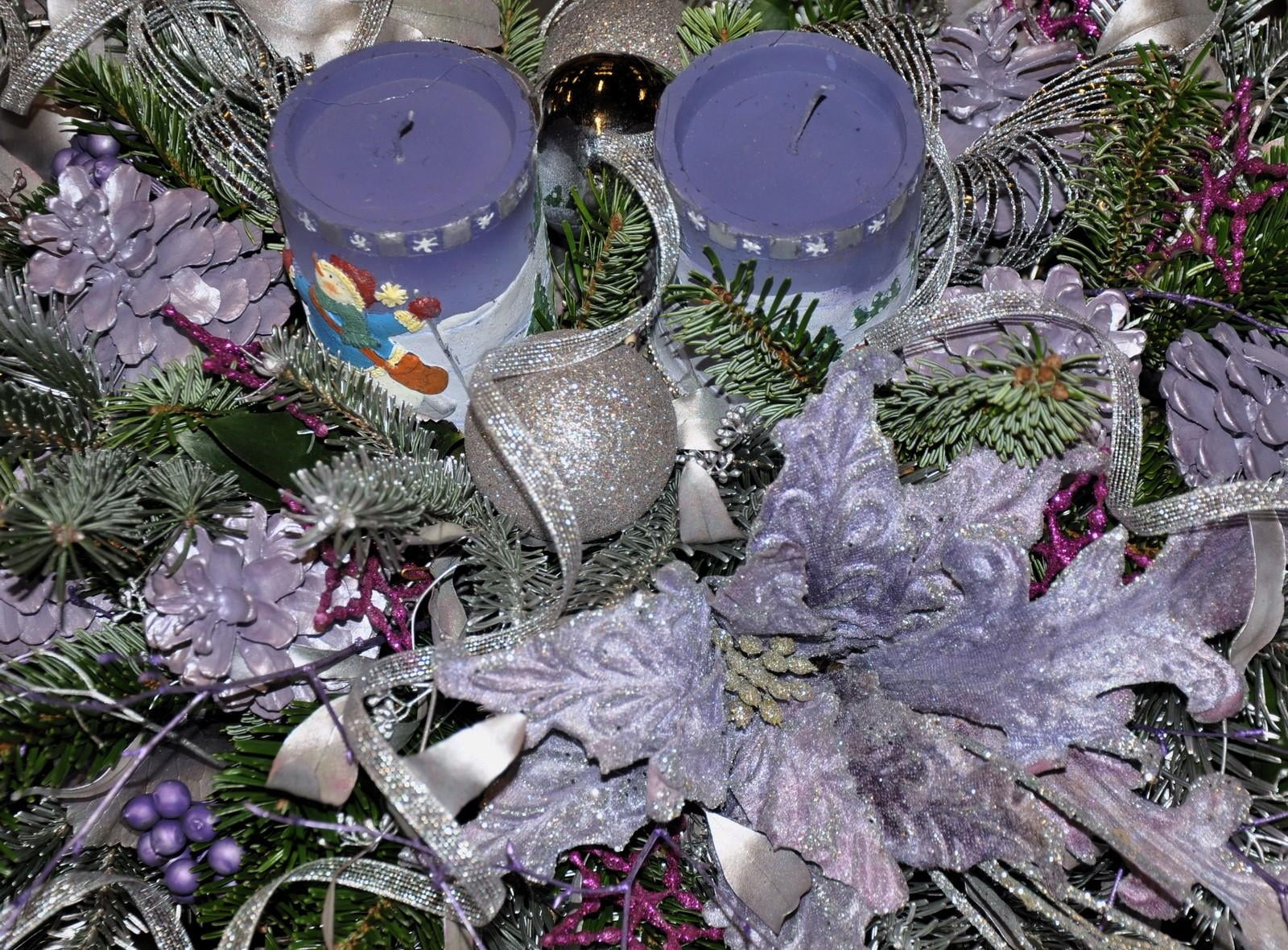 two purple pillar candle in middle of green wreath surrounded by pinecones and glittered Christmas baubles