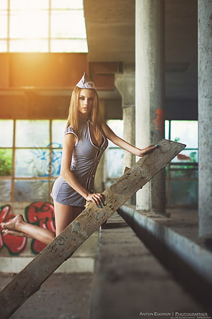 woman wearing gray nurse outfit climbing half way on wooden ladder posing for photo inside an abandoned building during photo shoot