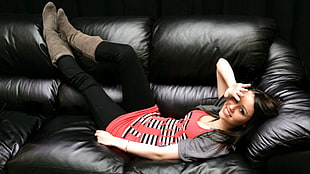 woman wearing red and black scoop-neck top and black pants lying on top of black leather 3-seat sofa