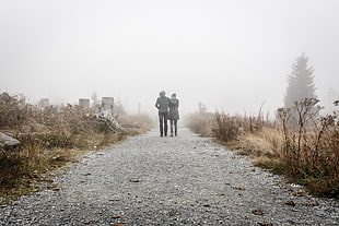 photo of couple wearing grey coat walking through broad path