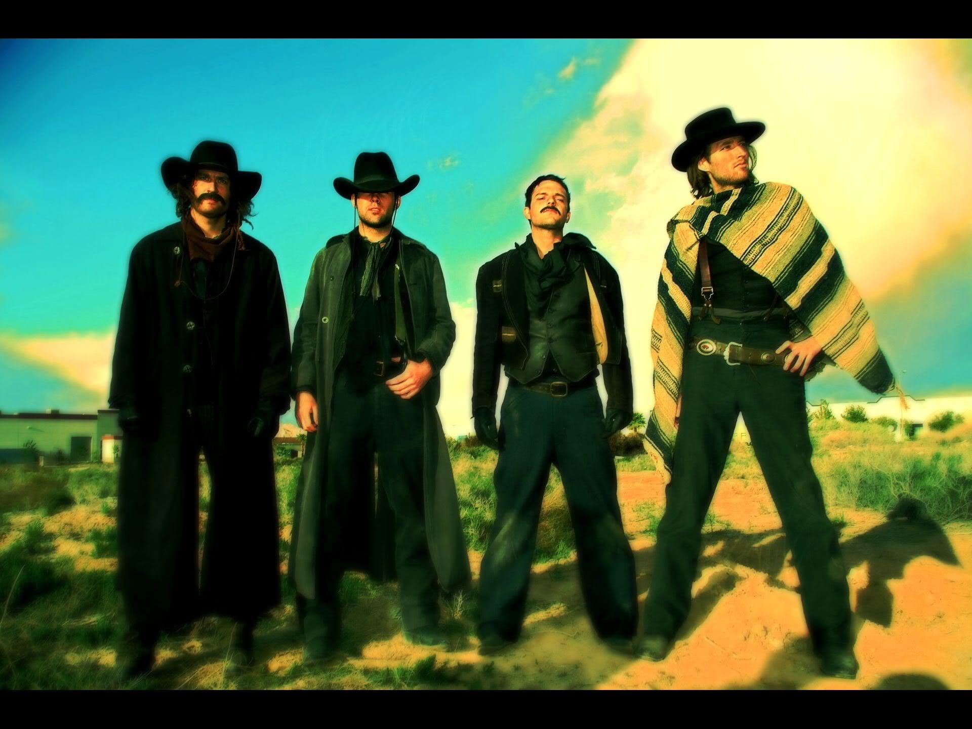 photo of four cowboys standing in desert dune during day time