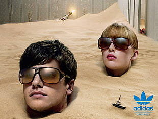 man and woman wearing sunglasses covered his/her body with brown sand