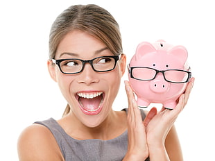woman wearing black framed eyeglasses holding pink piggy bank