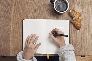 person holding black pen on right hand writing on white printer paper