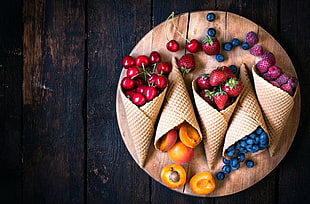 strawberry, blueberry, and red cherry with cones on top of round board