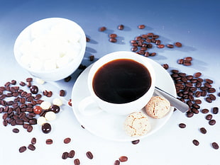 filled white ceramic cup on white saucer near teaspoon