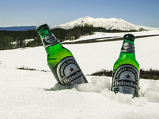 two Heineken beer bottles on white snow