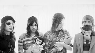 greyscale photo of four people standing hand holding monkey plush toy