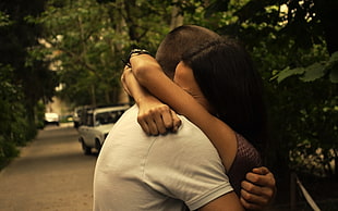 man in white shirt and woman in brown top hugging between road near white car
