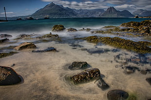 photo of rocks in body of water with mountains painting, elgol