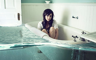 woman wearing white long-sleeved shirt sitting inside the white bath tub