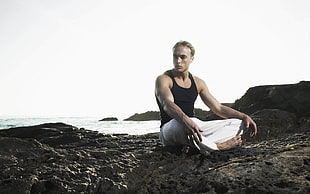 man in black tank top sitting on gray rocky shore