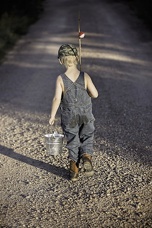 boy holding fishing rod and bucket walking towards empty road