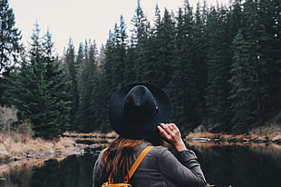 woman wearing gray long-sleeved shirt and black hat looking at river near trees