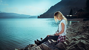 woman wearing white shirt and black denim jeans sitting on rocks in front of sea during daytime