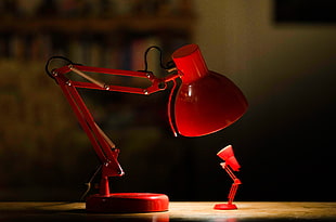 red desk lamp lighted on top of brown wooden surface