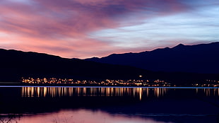reflection of city lights on body of water on mountain slope during sunset