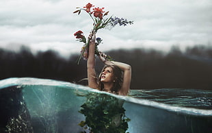 woman half submerged in water holding up a red flower half underwater photography