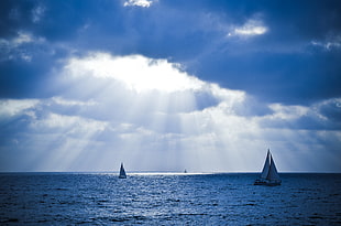 two sailboats on body of water under crepuscular rays