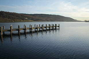 photo of brown wooden dock on body of water near mountain during day time