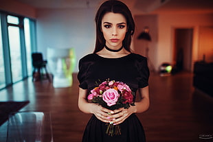 woman wears black scoop-neck dress holding pink flowers