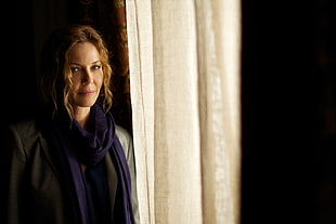 woman in blue scarf standing beside beige window curtain