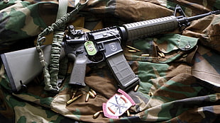 black and gray assault rifle on brown, black, and green camouflage textile