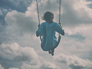 girl in white shirt sitting on swing under gray clouds