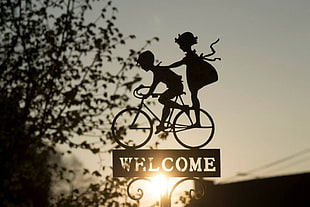silhouette of boy and girl riding bicycle cutout welcome signage