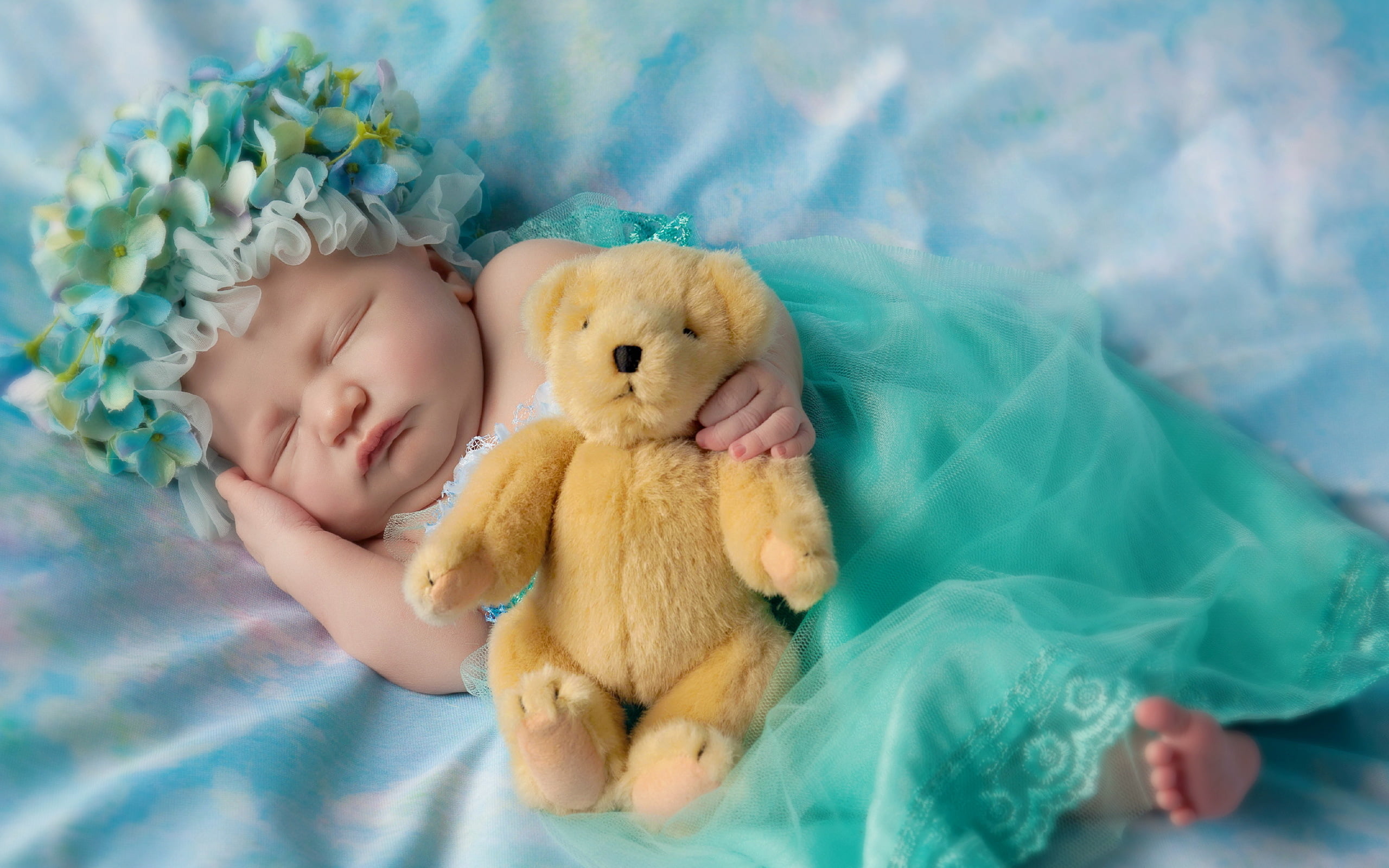 baby wearing white and green shirt holding brown bear